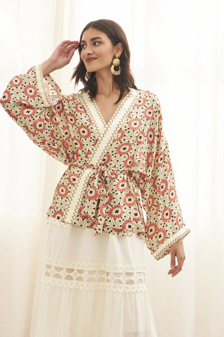 A woman wearing a stylish bohemian outfit, featuring a floral patterned kimono with wide sleeves and a white maxi skirt with lace detailing.