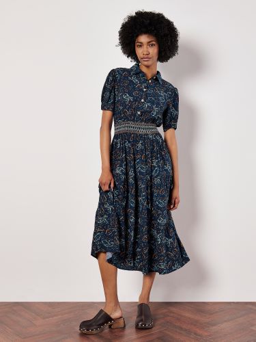 A person wearing a mid-length dress with an apricot paisley pattern, short sleeves, and a cinched waist with a belt detail. The dress has a flared skirt and is paired with dark-colored shoes.